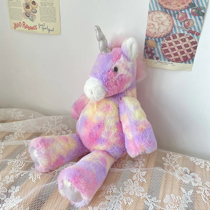 Pastel-colored teddy bear with a unicorn horn on a lace surface.