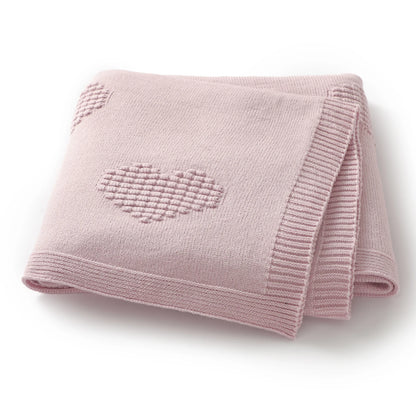 Pink knitted blanket with a heart design on a white background