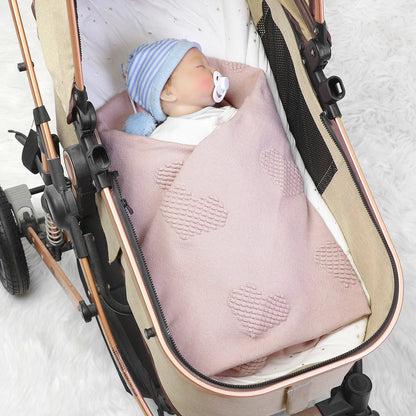 Baby wrapped in a pink blanket inside a stroller on a light background