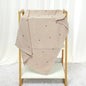 Beige knit blanket with colorful dots draped over a wooden crib against a white curtain background.