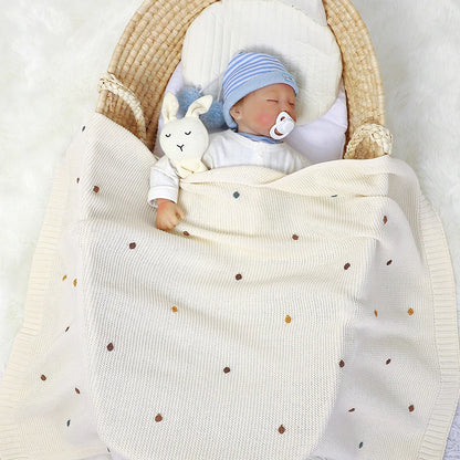 Newborn baby in a basket with a white blanket, blue hat, and rabbit plush toy.