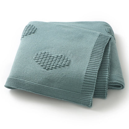 Folded teal / green knitted blanket with heart patterns on a white background