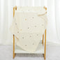 Beige blanket with colorful polka dots draped over a wooden chair against a white curtain background.