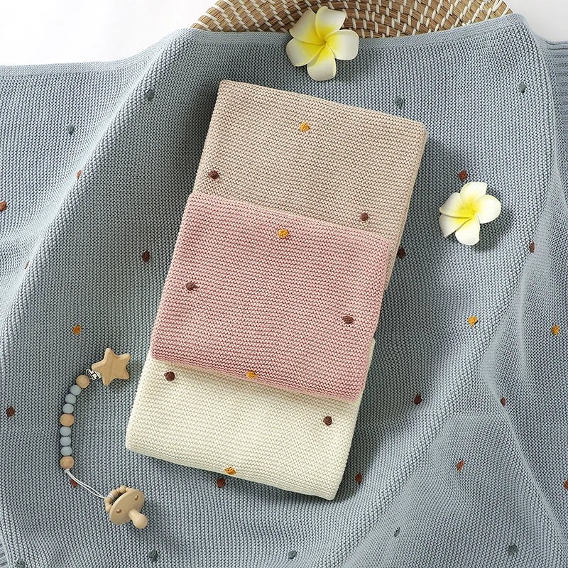 Stack of folded baby blankets with decorative flowers and a teething toy on a textured surface.