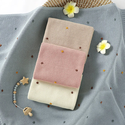 Stack of folded baby blankets with decorative flowers and a teething toy on a textured surface.