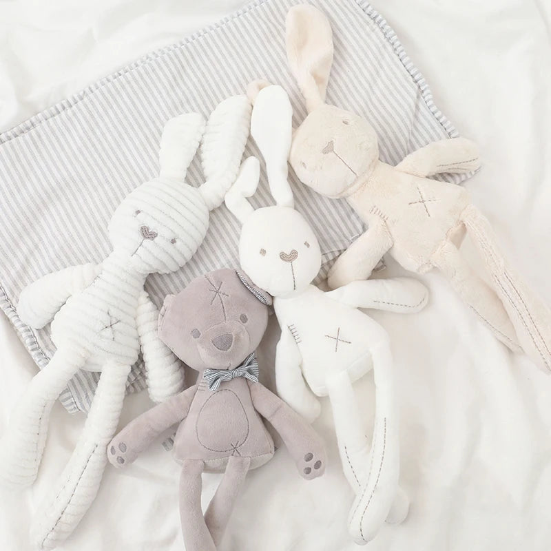 Collection of soft toys including bunnies and a bear on a textured fabric background
