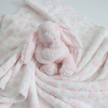Pink plush toy wrapped in a matching pink blanket with white polka dots on a light gray background