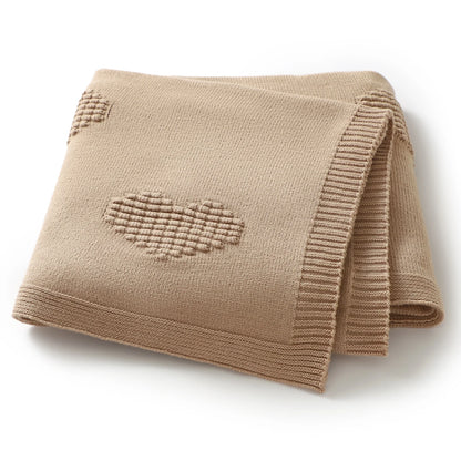 Folded beige blanket with a heart pattern on a white background
